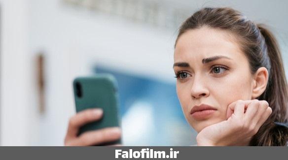 عکس یک زن که با نگرانی به تلفن همراهش نگاه میکند